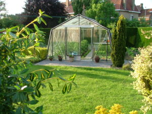Serre de jardin en verre et aluminium intégrée dans un jardin paysager